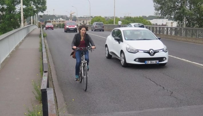 Une cycliste au bord de la route sans piste cyclable