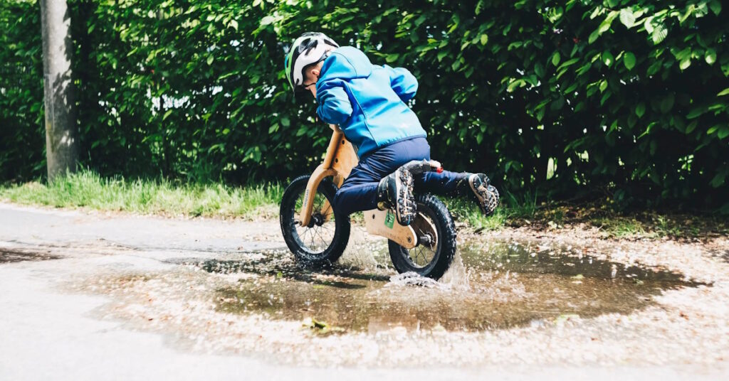 Un enfant qui traverse une flaque d'eau sur une draisienne en bois