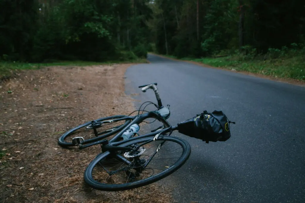 Un vélo de route posé au sol sur la route devant une forêt