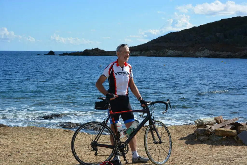 Un cycliste au bord de la Mer Méditerranée au pied d'une montagne en Corse