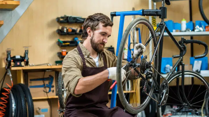 Un mécanicien vélo dans son garage en train de réparer une roue arrière avec une pince à la main