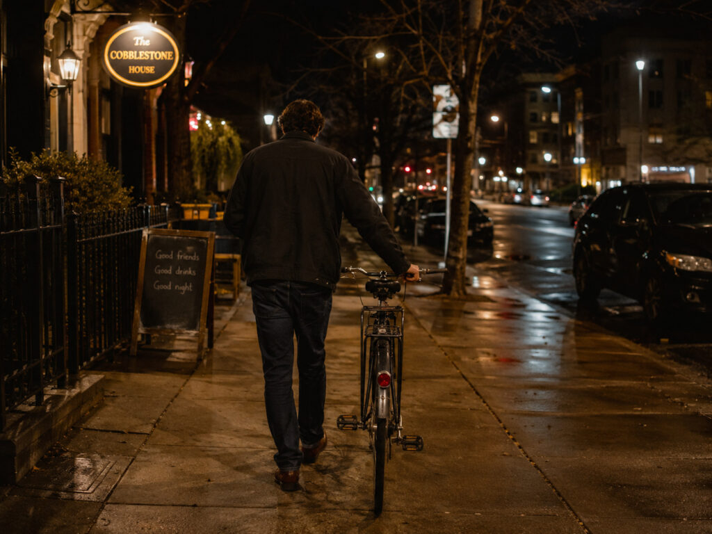 Un cycliste ayant bu qui rentre à pied à côté de son vélo la nuit